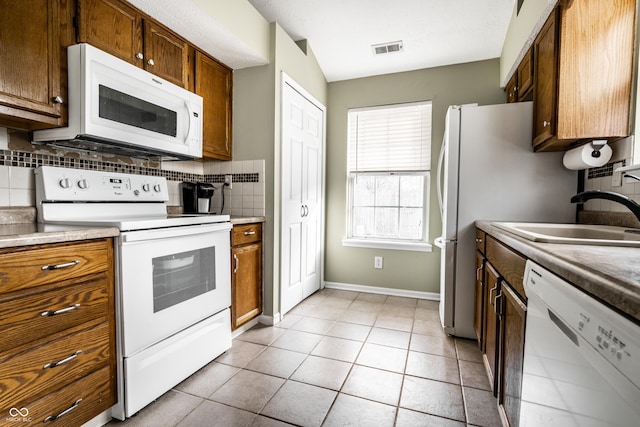 kitchen with light tile patterned flooring, white appliances, sink, and backsplash