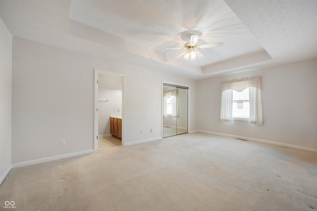 unfurnished bedroom with connected bathroom, light carpet, a closet, a raised ceiling, and ceiling fan