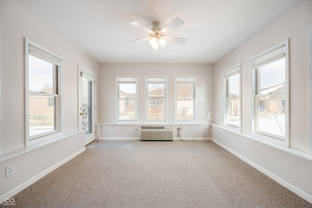 unfurnished sunroom with ceiling fan, a wealth of natural light, and an AC wall unit