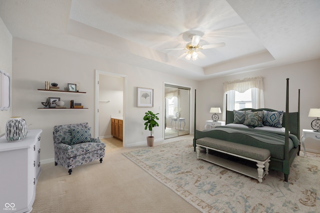 bedroom with ceiling fan, light colored carpet, a tray ceiling, a textured ceiling, and connected bathroom