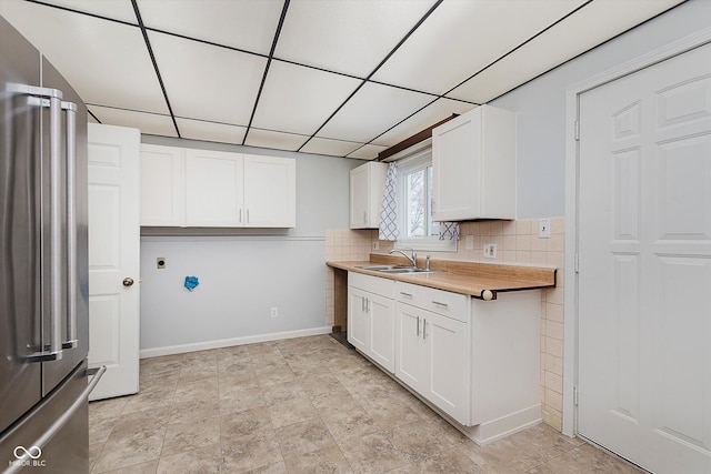 kitchen featuring sink, high end refrigerator, white cabinets, backsplash, and a drop ceiling