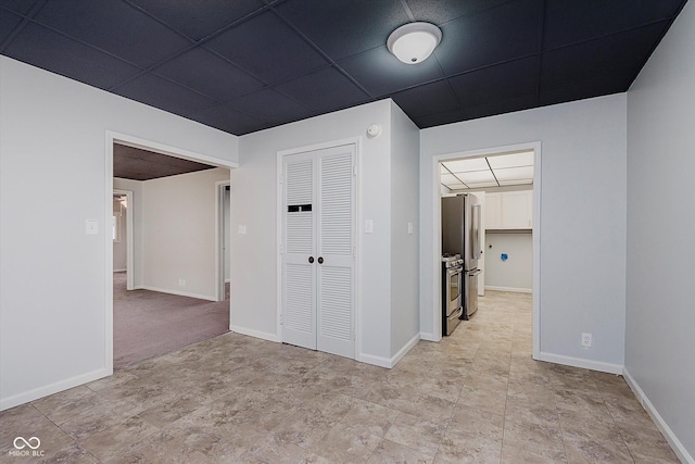 unfurnished bedroom with freestanding refrigerator, a closet, a drop ceiling, and baseboards