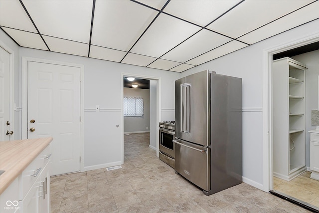 kitchen featuring a paneled ceiling, white cabinetry, baseboards, light countertops, and appliances with stainless steel finishes