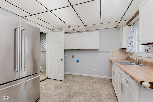 kitchen with high end refrigerator, white cabinets, decorative backsplash, light countertops, and a sink