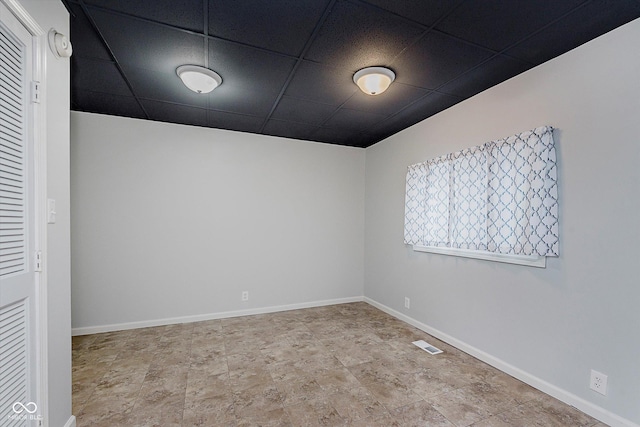 spare room with a paneled ceiling, visible vents, and baseboards