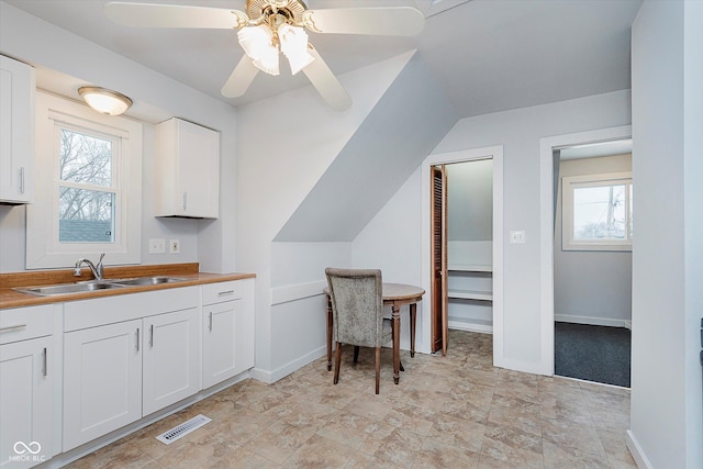 kitchen featuring visible vents, a ceiling fan, white cabinetry, a sink, and baseboards