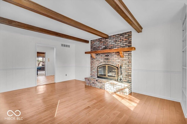 unfurnished living room with visible vents, beamed ceiling, a fireplace, and wood finished floors