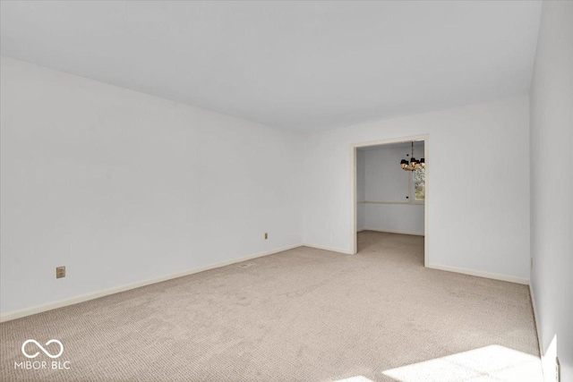 carpeted spare room featuring a notable chandelier and baseboards