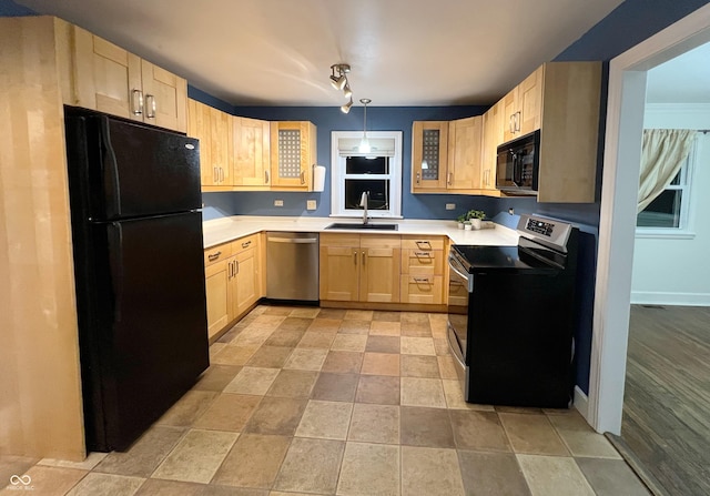 kitchen with a sink, hanging light fixtures, light brown cabinetry, light countertops, and black appliances