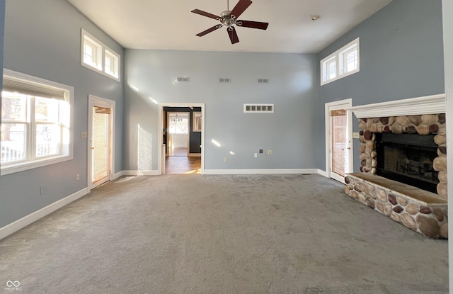 unfurnished living room featuring visible vents, a stone fireplace, carpet flooring, and a towering ceiling