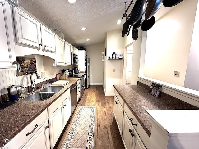 kitchen with dark wood-type flooring, sink, a textured ceiling, stainless steel appliances, and white cabinets