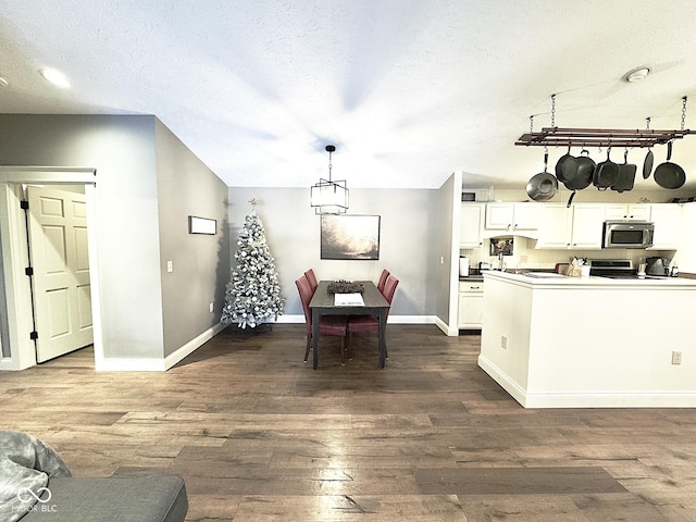 kitchen with appliances with stainless steel finishes, white cabinetry, a textured ceiling, dark hardwood / wood-style flooring, and decorative light fixtures