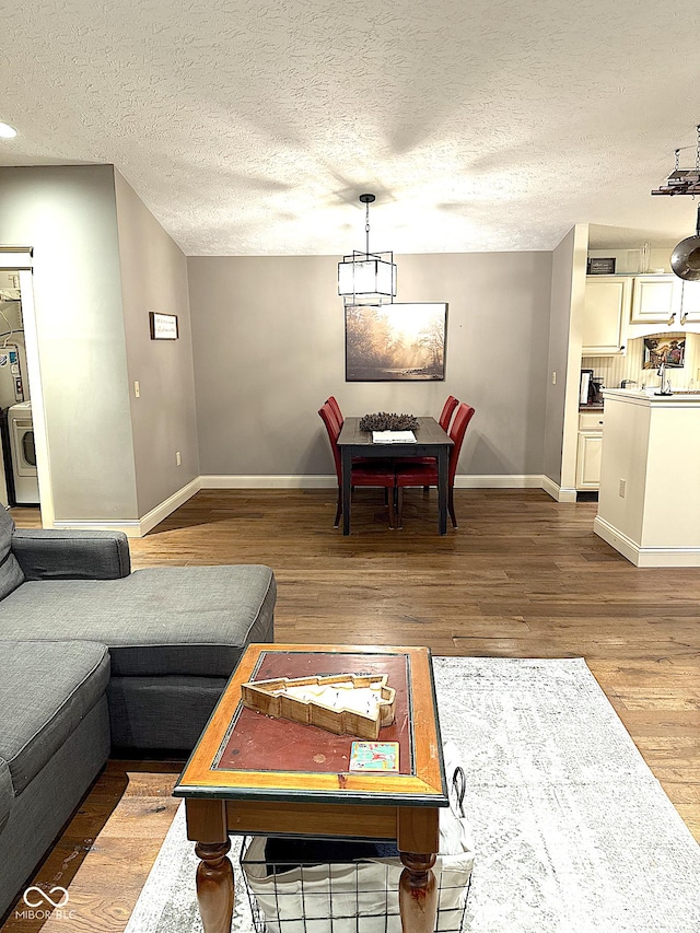 living room with washer / clothes dryer, a textured ceiling, baseboards, and wood finished floors