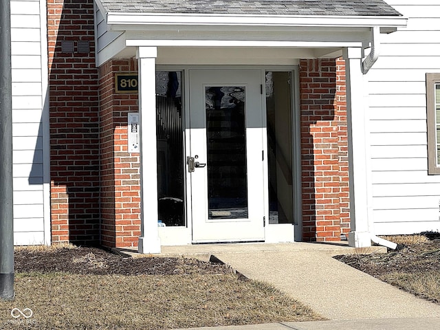 property entrance with a shingled roof and brick siding