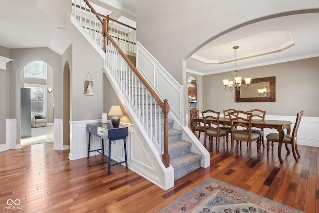 stairs with a raised ceiling, a high ceiling, hardwood / wood-style floors, and a chandelier