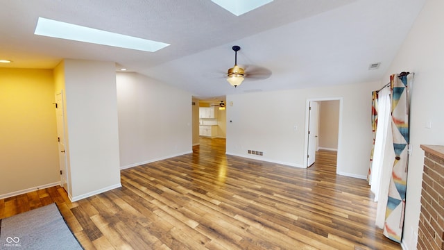 unfurnished living room featuring ceiling fan, hardwood / wood-style flooring, and vaulted ceiling with skylight