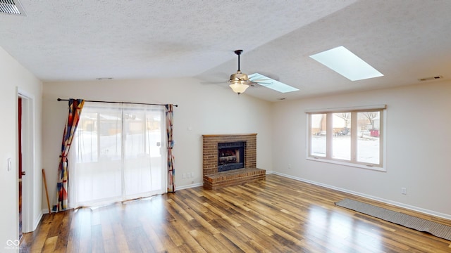 unfurnished living room featuring vaulted ceiling with skylight, hardwood / wood-style floors, a fireplace, ceiling fan, and a textured ceiling