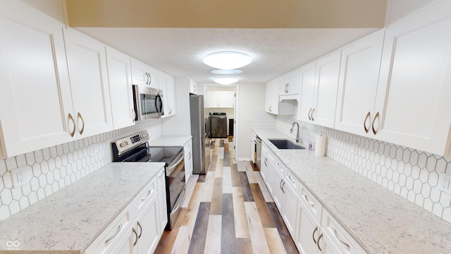 kitchen with sink, white cabinetry, light stone counters, a textured ceiling, and stainless steel appliances