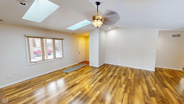 unfurnished room with ceiling fan, hardwood / wood-style flooring, a textured ceiling, and vaulted ceiling with skylight