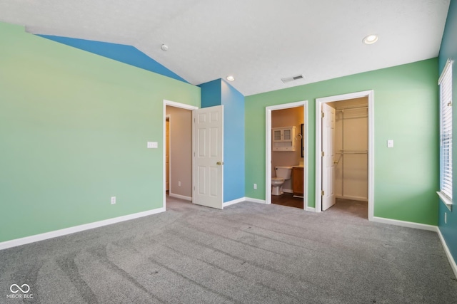 unfurnished bedroom featuring ensuite bathroom, a spacious closet, a closet, carpet, and lofted ceiling