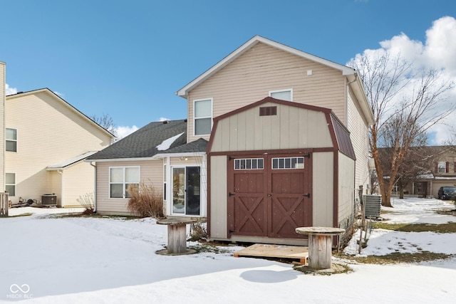 snow covered house featuring central air condition unit and a garage