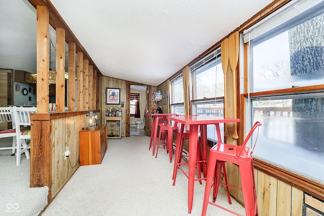 carpeted dining space featuring wooden walls and a textured ceiling