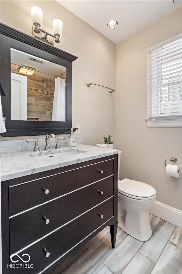 bathroom featuring vanity, wood finished floors, baseboards, visible vents, and toilet