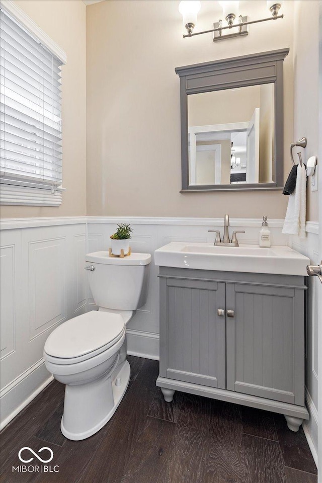 half bath with wainscoting, toilet, vanity, and wood finished floors