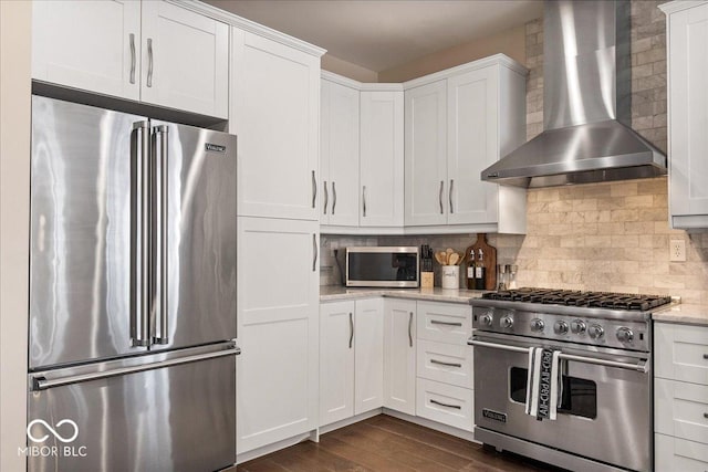 kitchen featuring decorative backsplash, white cabinetry, high quality appliances, and wall chimney range hood