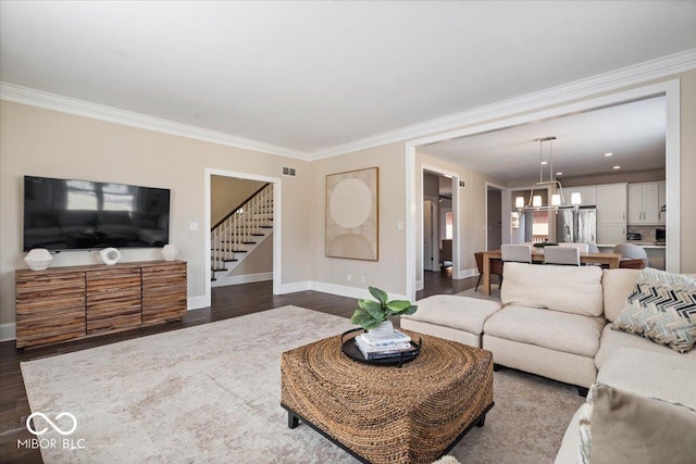 living room featuring ornamental molding, stairs, an inviting chandelier, baseboards, and dark wood-style flooring