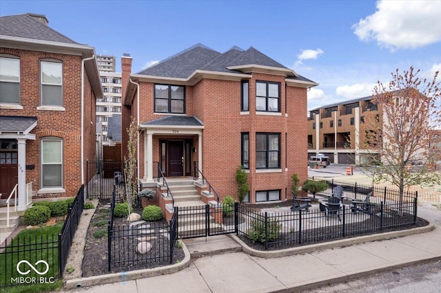 townhome / multi-family property featuring brick siding, a fenced front yard, and roof with shingles