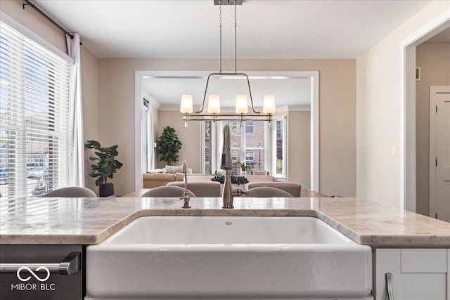 kitchen featuring a sink, decorative light fixtures, light stone counters, white cabinetry, and an inviting chandelier