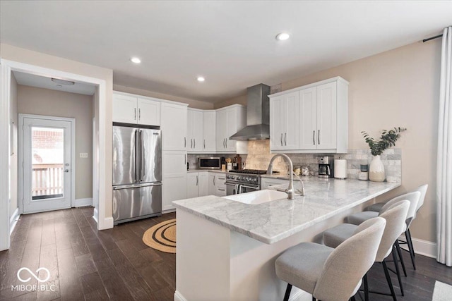 kitchen with a sink, tasteful backsplash, a peninsula, wall chimney range hood, and high end appliances