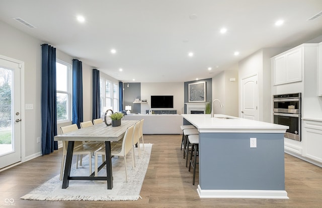 kitchen featuring light countertops, double oven, a kitchen island with sink, and white cabinets