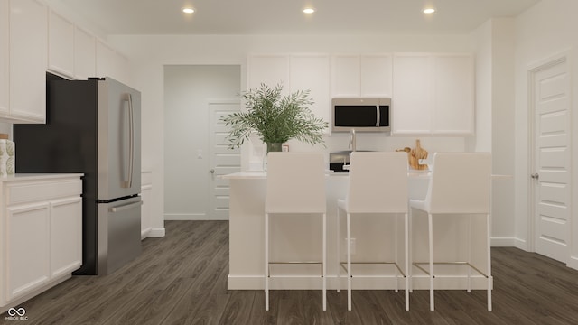 kitchen with white cabinetry, appliances with stainless steel finishes, dark hardwood / wood-style floors, and a breakfast bar area