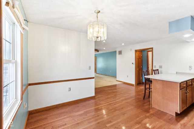 kitchen with light wood finished floors, baseboards, an inviting chandelier, light countertops, and a kitchen bar