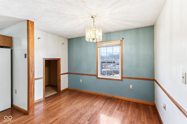 spare room with an inviting chandelier, wood finished floors, visible vents, and baseboards