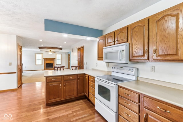 kitchen with white appliances, light countertops, a fireplace, and a peninsula