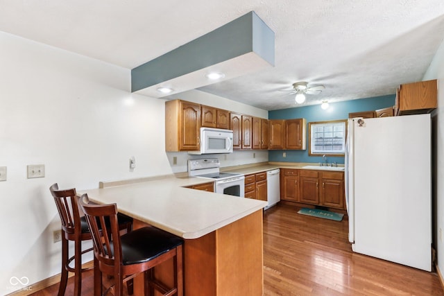 kitchen featuring ceiling fan, a peninsula, white appliances, a sink, and brown cabinets