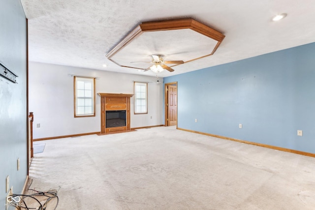 unfurnished living room with ceiling fan, a textured ceiling, baseboards, carpet, and a glass covered fireplace