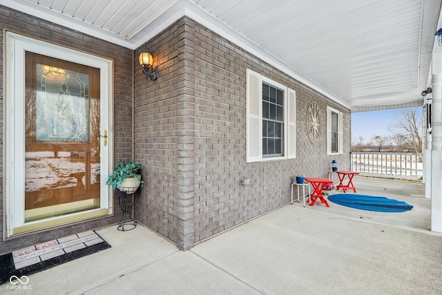 doorway to property with covered porch and brick siding