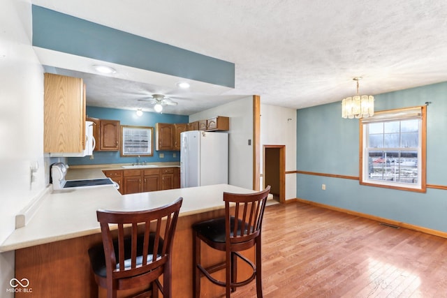 kitchen featuring light wood-style flooring, a peninsula, white appliances, a sink, and light countertops