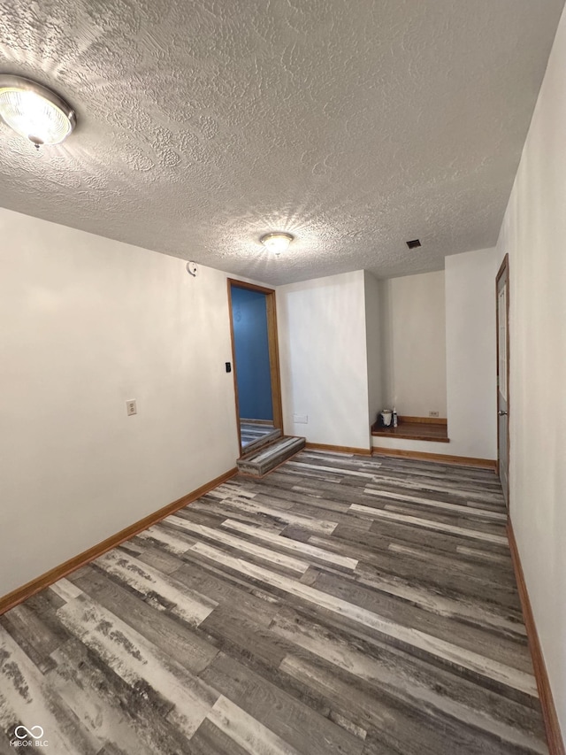 empty room featuring a textured ceiling, baseboards, and wood finished floors