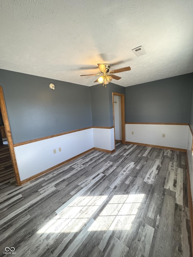 spare room featuring a ceiling fan, visible vents, a textured ceiling, and wood finished floors