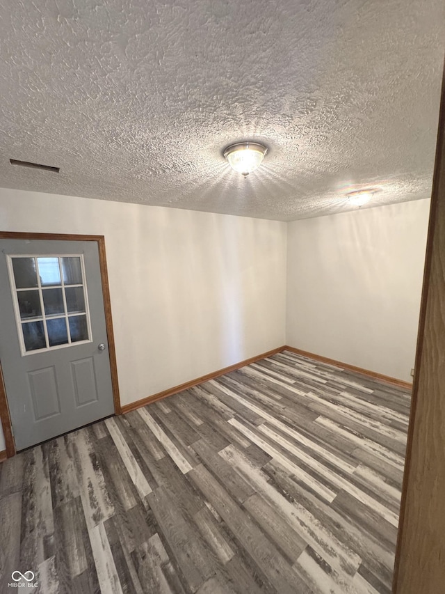 empty room with a textured ceiling, wood finished floors, and baseboards