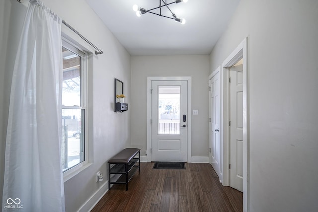 doorway to outside with plenty of natural light, dark wood-type flooring, and an inviting chandelier