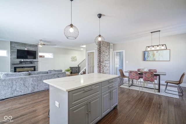 kitchen featuring gray cabinets, hanging light fixtures, dark hardwood / wood-style floors, light stone countertops, and a kitchen island