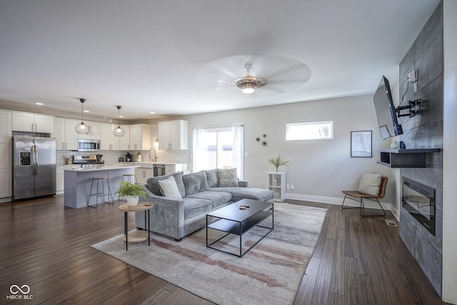 living room with ceiling fan, sink, a fireplace, and dark hardwood / wood-style flooring