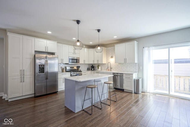 kitchen featuring decorative light fixtures, white cabinetry, dark hardwood / wood-style flooring, a center island, and stainless steel appliances