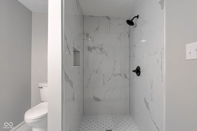 bathroom featuring toilet, tiled shower, and a textured ceiling